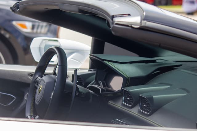 The interior of a luxury convertible car, focusing on the steering wheel and dashboard, with the top down