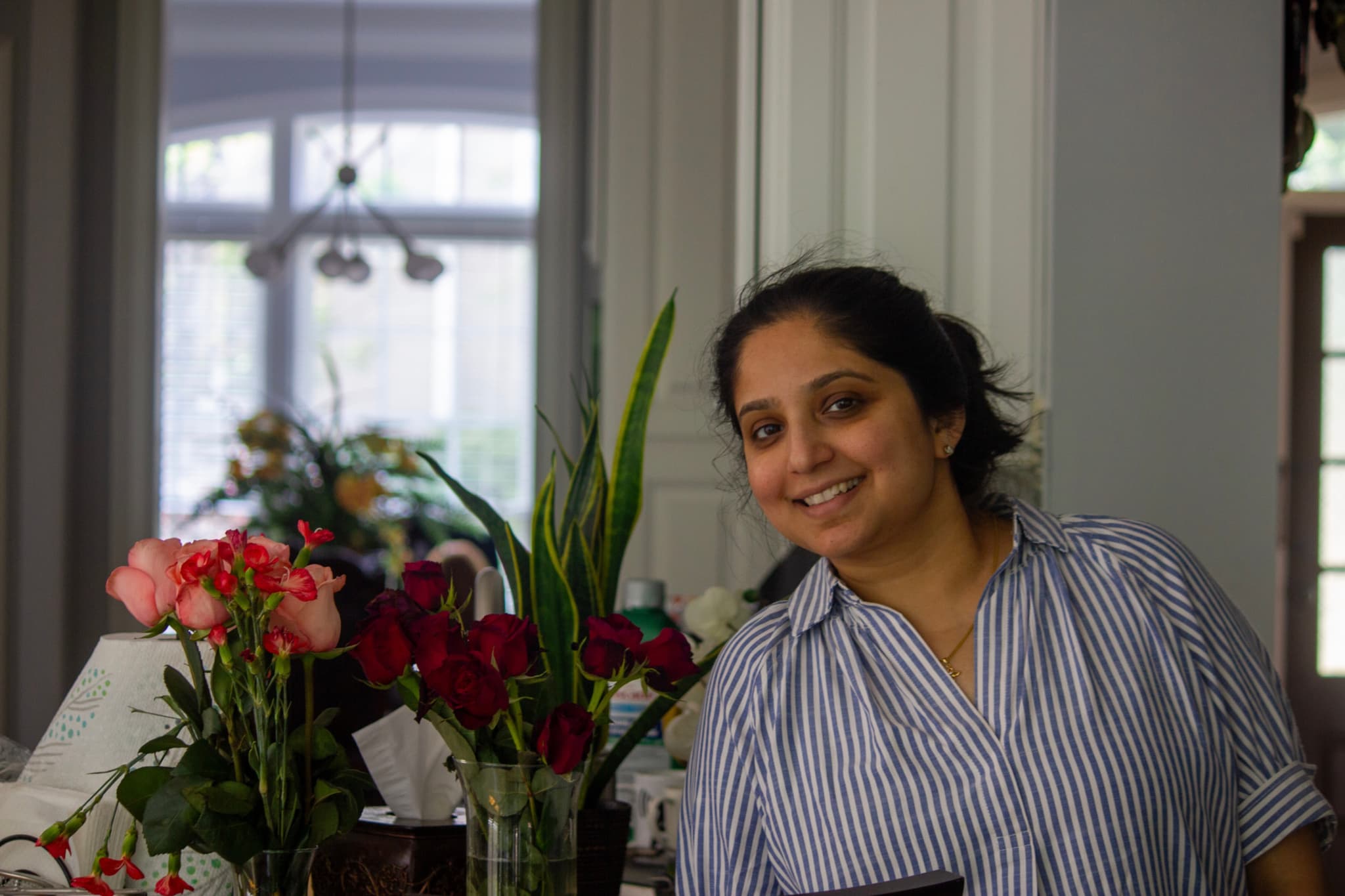 A person smiling in a room with various flowers and plants in the background