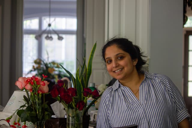A person smiling in a room with various flowers and plants in the background