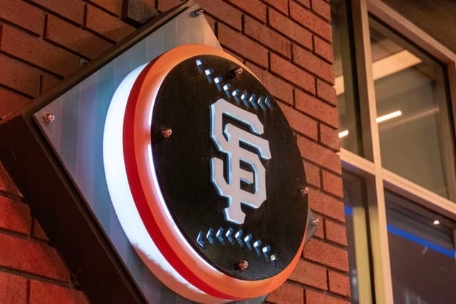 A circular sign with the letters SF in a stylized font, mounted on a brick wall, illuminated with a red and white border