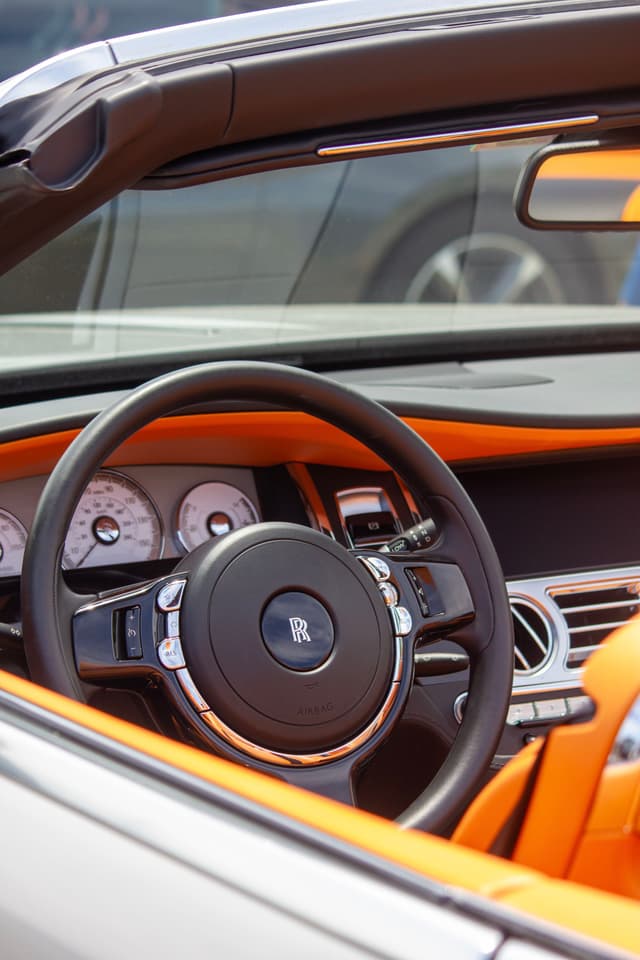 A luxury car interior with an orange and black color scheme, featuring a steering wheel with a prominent logo and a dashboard with multiple gauges